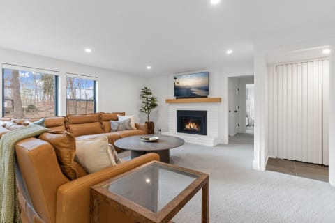Stylish living room featuring a tan leather sofa, white brick fireplace, and large windows.