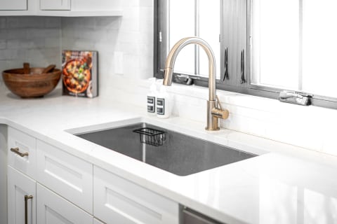 Modern kitchen sink with black basin, marble countertop, and bronze faucet.