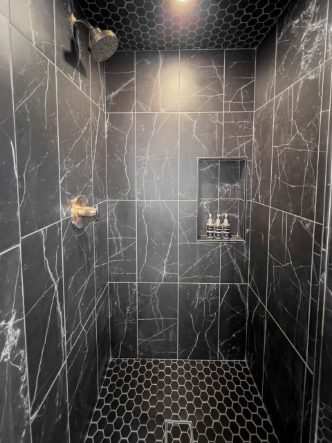 A sleek shower featuring dark marble tiles and hexagonal tile flooring.