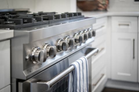 A close-up shot of a sleek stainless steel gas stove with knobs and a striped towel hanging.