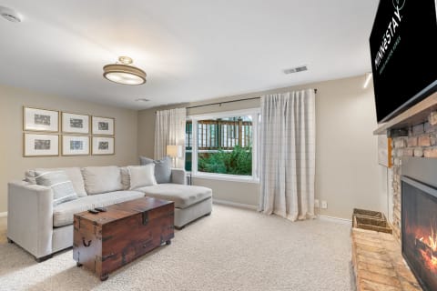 A light gray sectional sofa in a cozy living room, featuring a rustic trunk as a coffee table and large windows with white curtains.