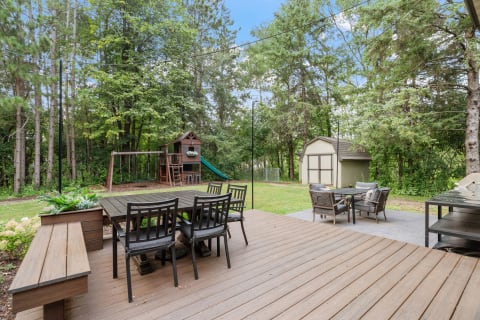 Outdoor deck with seating area, playground, and surrounding trees.
