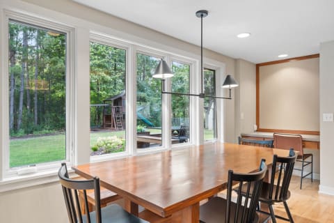 Cozy dining room with a wooden table, black chairs, and a view of trees outside.