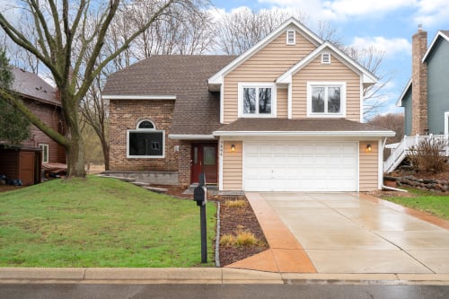 A charming two-story home with brick and siding exterior, featuring a welcoming red front door and convenient two-car garage in a quiet residential neighborhood.