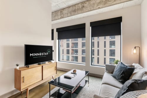 Relax in your stylish living room with exposed beams, modern furnishings, and bright city views through floor-to-ceiling windows.