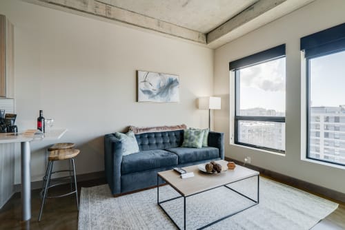 Relax in your stylish living space featuring a plush blue sofa, modern bar seating, and expansive city views from large windows.
